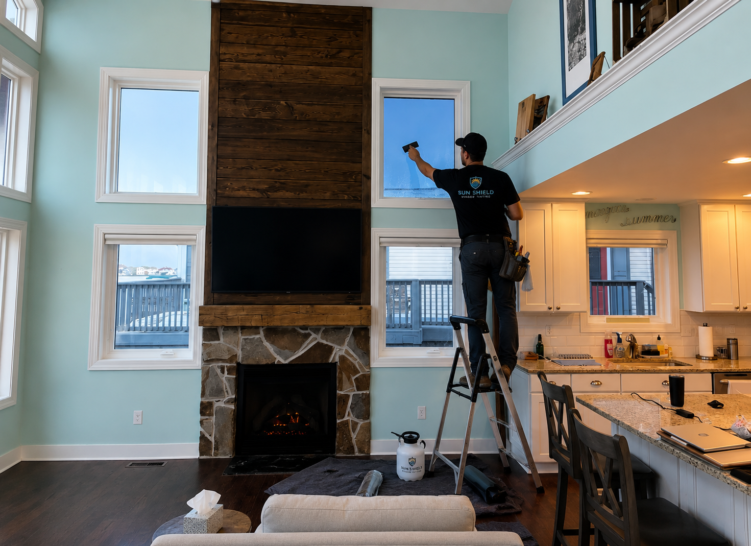 Window tinting installer on ladder applying film to tall residential windows